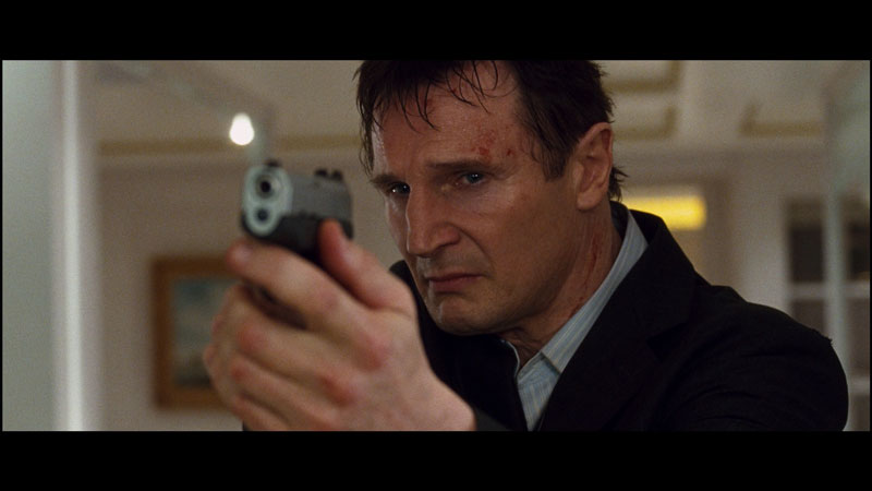 Liam Neeson from 'Taken' standing and holding a gun towards the camera