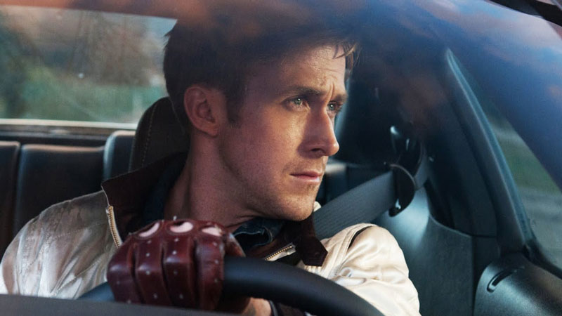 Ryan Gosling from 'Drive' holding his hand on the steering wheel with a red glove and looking into the distance.