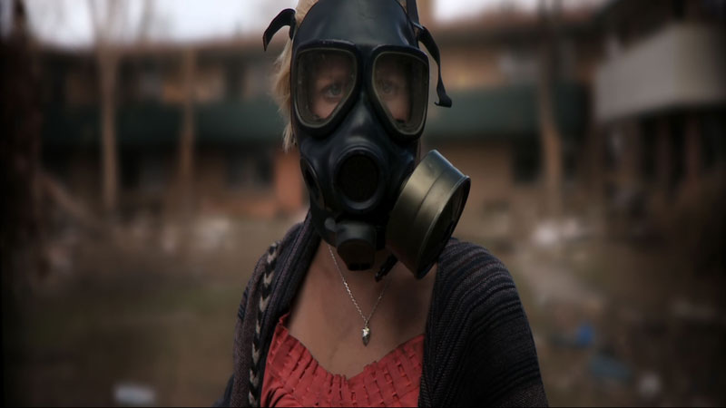 The lead actress from 'Monsters' looking towards the camera and wearing a gas mask