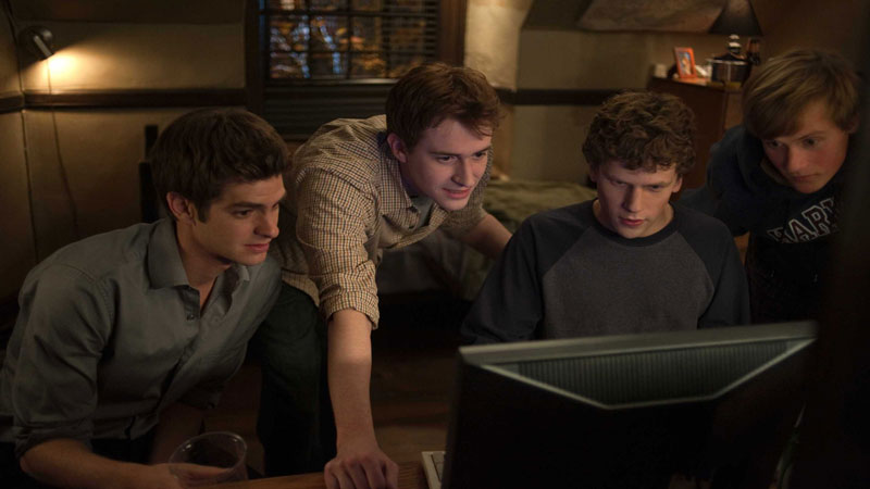 The primary cast of 'The Social Network' sitting and looking at a computer monitor