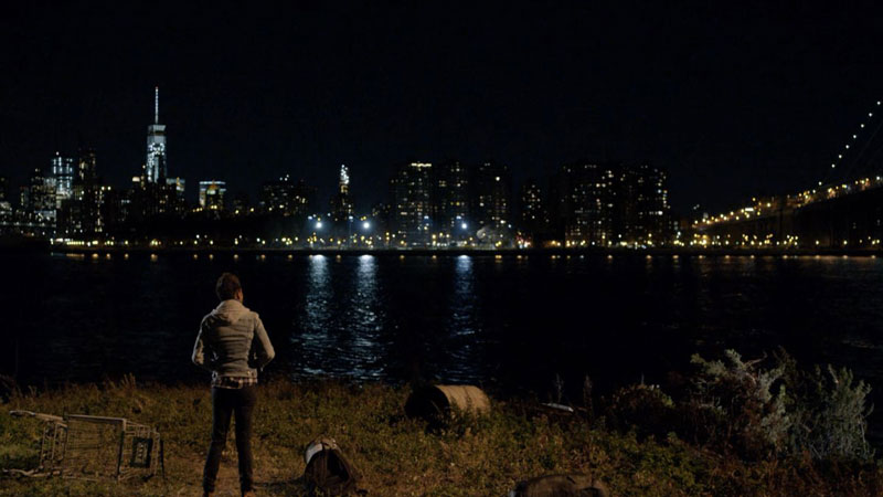 An actress from 'Orange is the New Black' on Netflix standing near water looks at a city at night